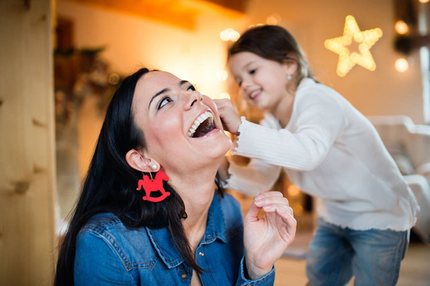 Young mother with daugter decorating Christmas tree together. - Foto, afbeelding