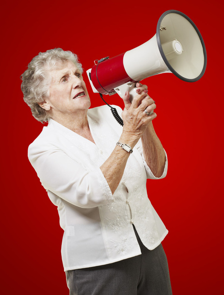 Portrait of senior woman holding megaphone over red background - Photo, Image