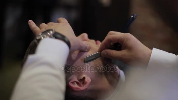 Człowiek po goleniu o fryzjera z bliska. Za pomocą maszynki z ostrym nożem i krem żel do cięcia włosy włosia wąsy na twarzy klienta profesjonalnego fryzjera. Szczęśliwy uśmiechający się zadowolony klient dla zakładów fryzjerskich - Materiał filmowy, wideo