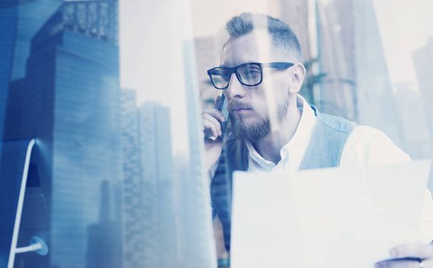 Bearded young businessman wearing white shirt,waistcoat and making call at the working place.Concept of successful business.Double exposure,skyscraper office building on blurred background. - Foto, Imagen