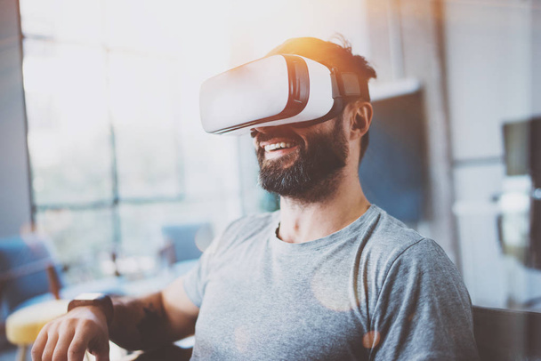 Bearded man wearing virtual reality glasses in modern interior design coworking studio. Smartphone using with VR goggles headset. Horizontal,film effect, blurred background. - Φωτογραφία, εικόνα