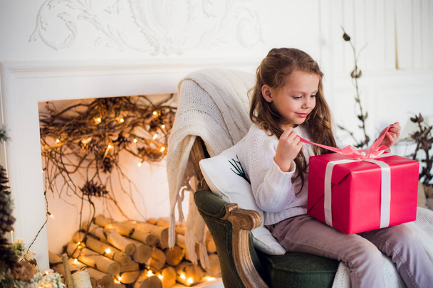 Onnellinen lapsi tyttö istuu nojatuoli peitetty huopa vastaan koristeltu joulun takka
 - Valokuva, kuva