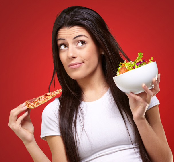 portrait of young woman choosing pizza or salad against a red ba - Photo, Image