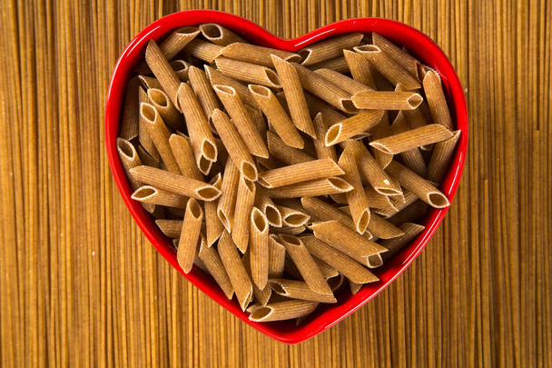 Wholemeal Pasta. Integral Penne into a heart bowl over a wooden  - Foto, Imagem