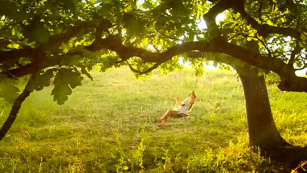 piękna dziewczyna na huśtawce w parku, lasu. gałęzie drzewa dębowe - Materiał filmowy, wideo
