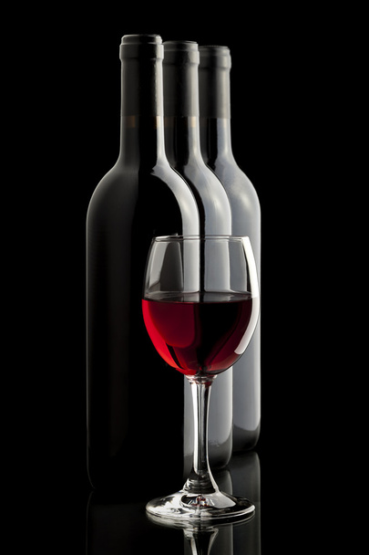 Κομψό κόκκινο ποτήρι κρασιού και μπουκάλια κρασιού σε μαύρο φόντο - Φωτογραφία, εικόνα