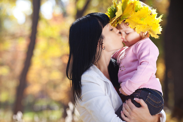 beautiful young mother kissing her daughter in autumn forest - Fotó, kép