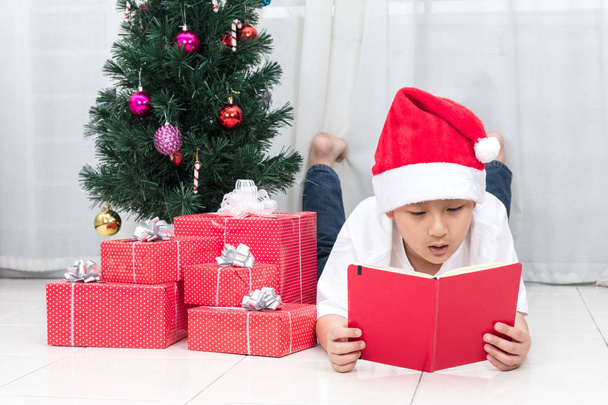Asian Chinese little boy reading book beside Christmas presents - Фото, зображення