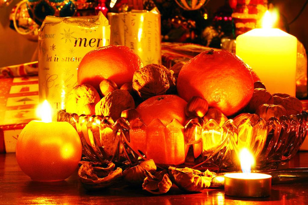 Стеклянная чаша, наполненная грецкими орехами, фундуком и мандариновыми апельсинами с рождественскими подарками в задней части, Англия
. - Фото, изображение