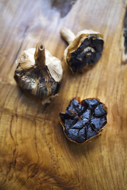 Bulbos y dientes de ajo negro sobre fondo de madera
 - Foto, imagen