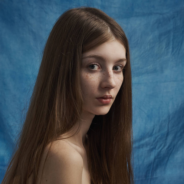 Szépség téma: egy szép, fiatal lány a szeplő arcát, és egy fekete ruhát visel kék háttérrel stúdióban portré - Fotó, kép