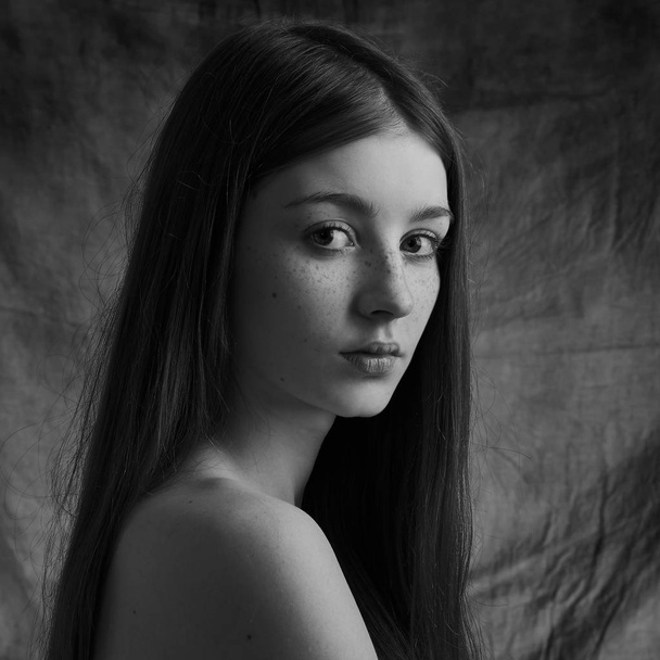 Dramatic black and white portrait of a beautiful lonely girl with freckles isolated on a dark background in studio shot - Foto, Imagen