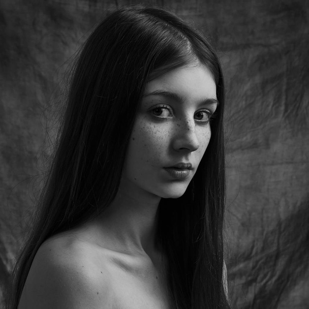 Dramatic black and white portrait of a beautiful lonely girl with freckles isolated on a dark background in studio shot - Foto, immagini