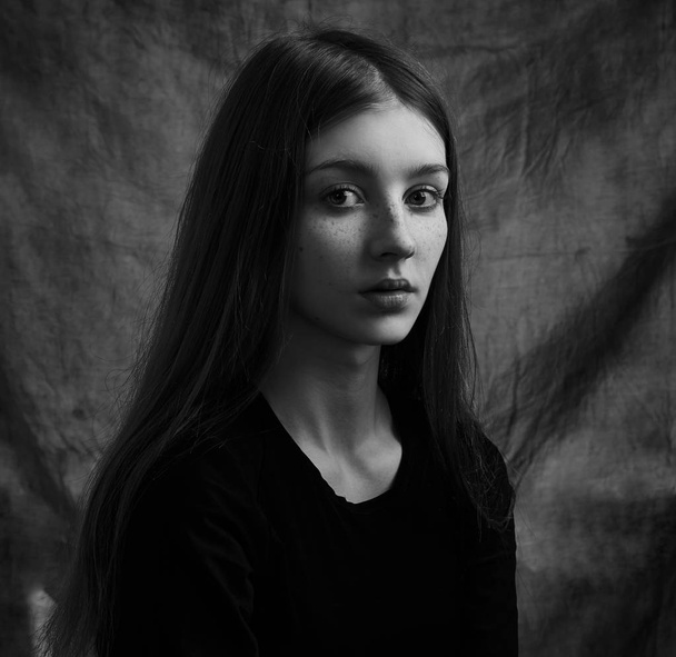Dramatic black and white portrait of a beautiful lonely girl with freckles isolated on a dark background in studio shot - Fotó, kép