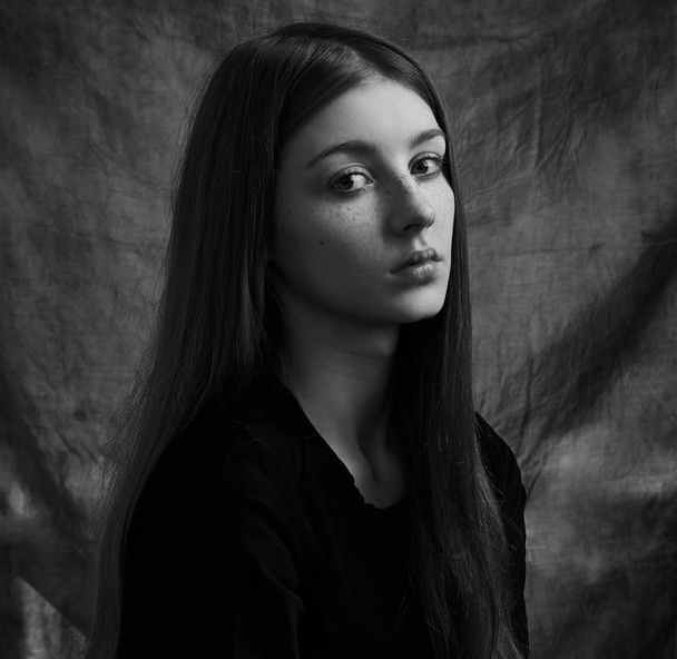 Dramatic black and white portrait of a beautiful lonely girl with freckles isolated on a dark background in studio shot - Foto, Imagem