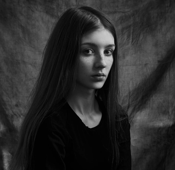 Dramatic black and white portrait of a beautiful lonely girl with freckles isolated on a dark background in studio shot - Foto, imagen