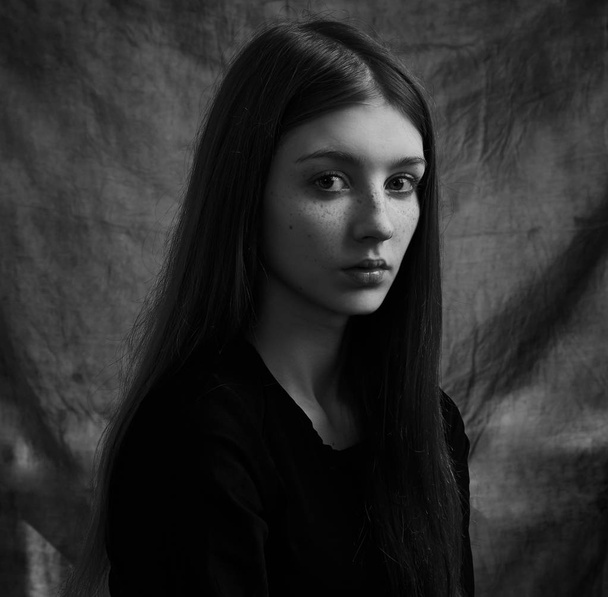Dramatic black and white portrait of a beautiful lonely girl with freckles isolated on a dark background in studio shot - Photo, Image