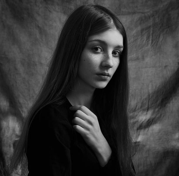 Dramatic black and white portrait of a beautiful lonely girl with freckles isolated on a dark background in studio shot - 写真・画像