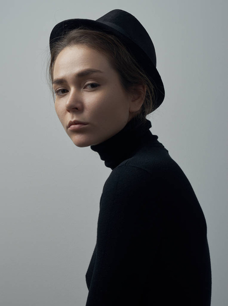 Dramatic portrait of a young beautiful girl with freckles in a black turtleneck and a hat on her head on a white background in studio - Foto, immagini