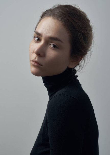 Dramatic portrait of a young beautiful girl with freckles in a black turtleneck on white background in studio - 写真・画像
