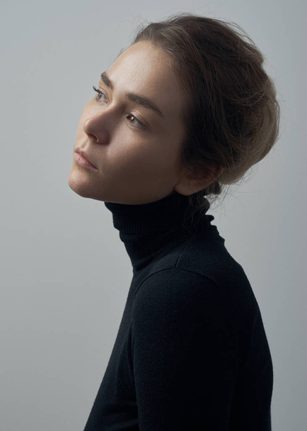 Dramatic portrait of a young beautiful girl with freckles in a black turtleneck on white background in studio - Zdjęcie, obraz