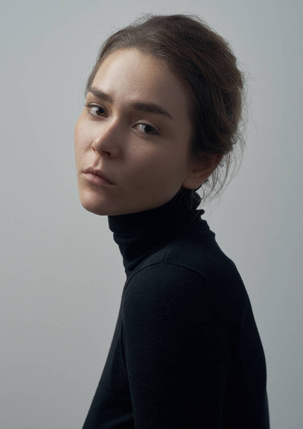 Dramatic portrait of a young beautiful girl with freckles in a black turtleneck on white background in studio - Foto, imagen