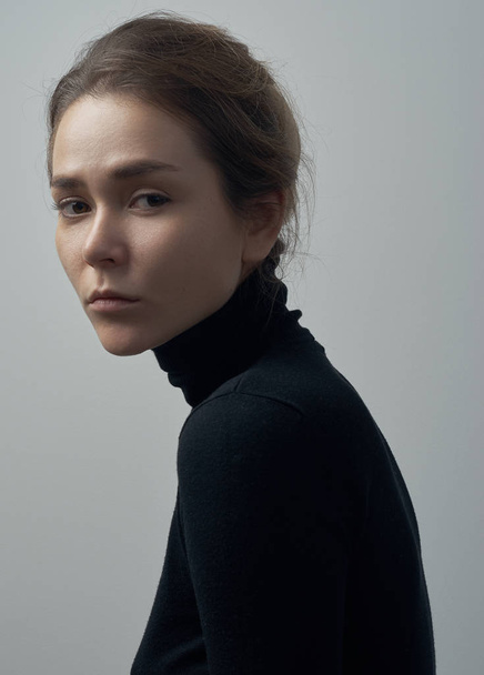 Dramatic portrait of a young beautiful girl with freckles in a black turtleneck on white background in studio - Фото, зображення