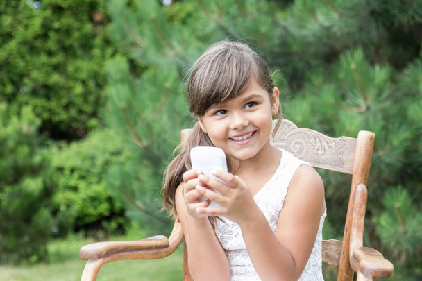 Smiling brunette little girl with smart phone outdoors - Φωτογραφία, εικόνα
