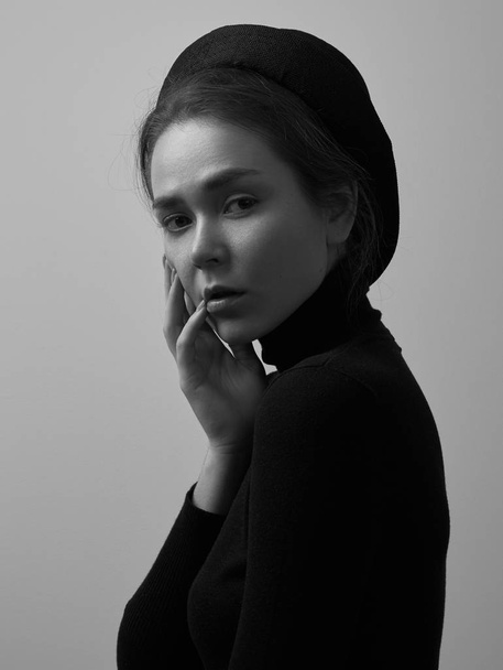 Dramatic black and white portrait of young beautiful girl with freckles in a black turtleneck and a hat on a white background in studio - Fotografie, Obrázek