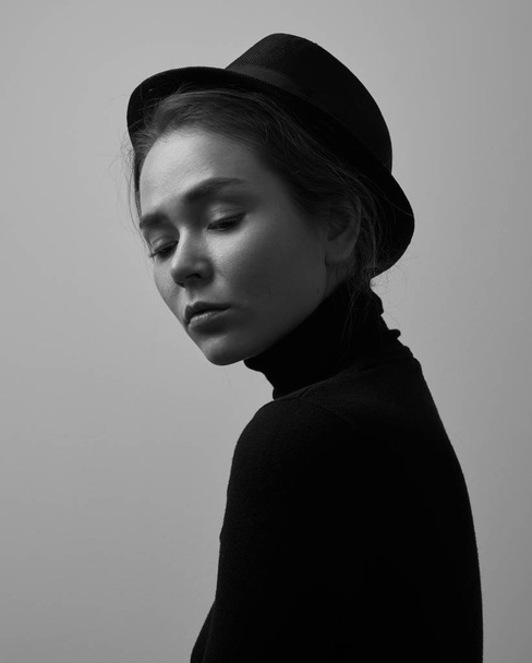 Dramatic black and white portrait of young beautiful girl with freckles in a black turtleneck and a hat on a white background in studio - Foto, imagen