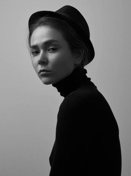 Dramatic black and white portrait of young beautiful girl with freckles in a black turtleneck and a hat on a white background in studio - Valokuva, kuva
