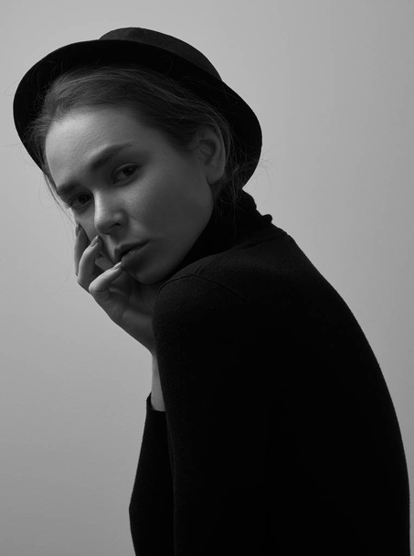 Dramatic black and white portrait of young beautiful girl with freckles in a black turtleneck and a hat on a white background in studio - Photo, Image