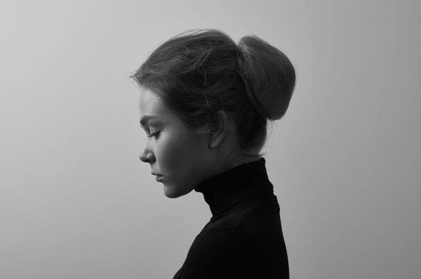 Dramatic black and white portrait of young beautiful girl with freckles in a black turtleneck on white background in studio - Foto, afbeelding