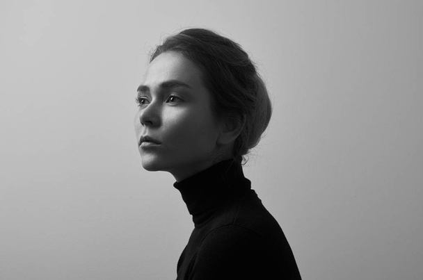 Dramatic black and white portrait of young beautiful girl with freckles in a black turtleneck on white background in studio - Zdjęcie, obraz