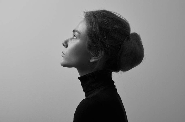 Dramatic black and white portrait of young beautiful girl with freckles in a black turtleneck on white background in studio - Fotografie, Obrázek