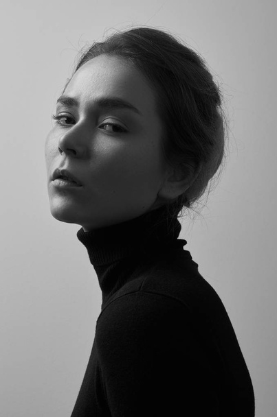 Dramatic black and white portrait of young beautiful girl with freckles in a black turtleneck on white background in studio - Photo, Image