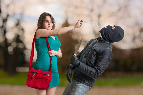 Молода жінка бореться з розпилювачем перцю проти озброєного злодія ножем
. - Фото, зображення