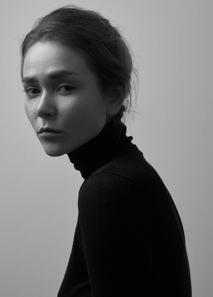 Dramatic black and white portrait of young beautiful girl with freckles in a black turtleneck on white background in studio - Foto, immagini