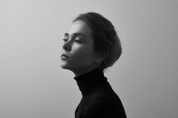 Dramatic black and white portrait of young beautiful girl with freckles in a black turtleneck on white background in studio - Fotoğraf, Görsel