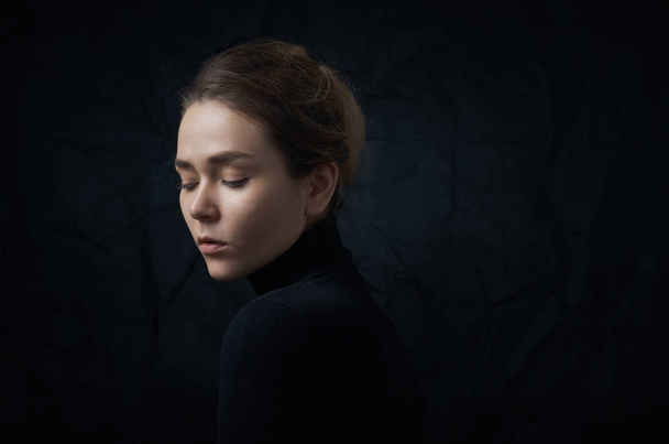 Dramatic portrait of a young beautiful girl with freckles in a black turtleneck on black background in studio - Photo, Image