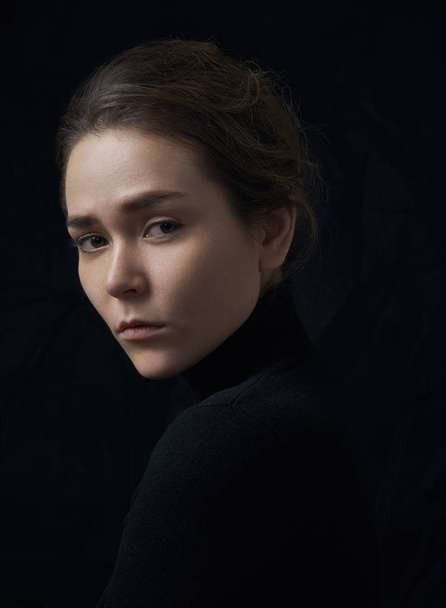 Dramatic portrait of a young beautiful girl with freckles in a black turtleneck on black background in studio - Fotografie, Obrázek