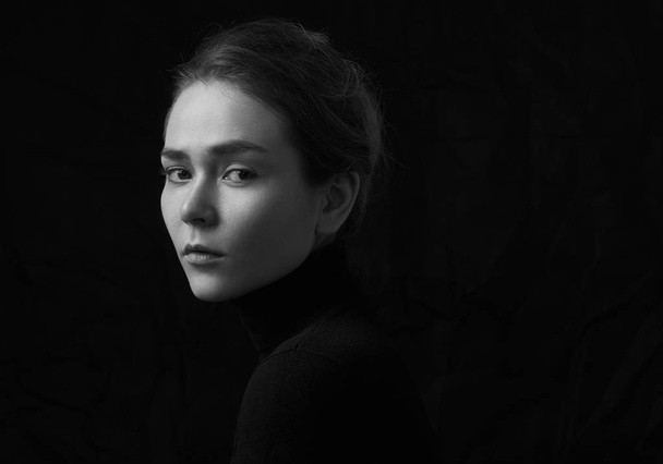 Dramatic black and white portrait of young beautiful girl with freckles in a black turtleneck on black background in studio - Fotografie, Obrázek