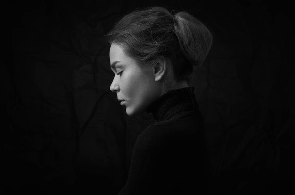Dramatic black and white portrait of young beautiful girl with freckles in a black turtleneck on black background in studio - Foto, imagen