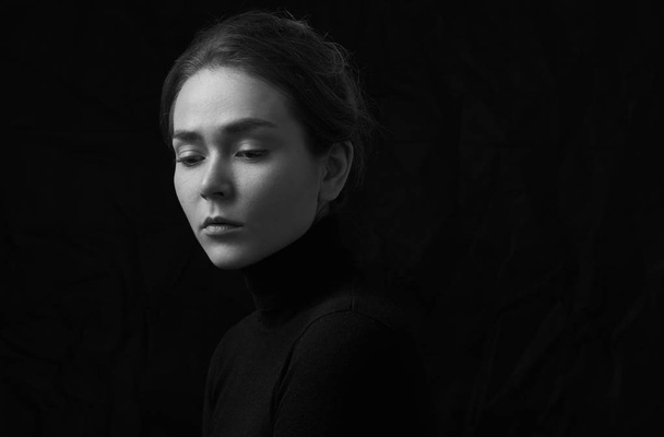Dramatic black and white portrait of young beautiful girl with freckles in a black turtleneck on black background in studio - Фото, изображение