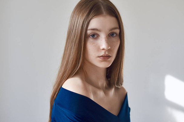 Beauty theme: portrait of a beautiful young girl with freckles on her face and wearing a blue dress on a white background in studio - Photo, Image
