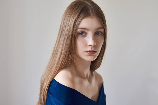Beauty theme: portrait of a beautiful young girl with freckles on her face and wearing a blue dress on a white background in studio - Zdjęcie, obraz