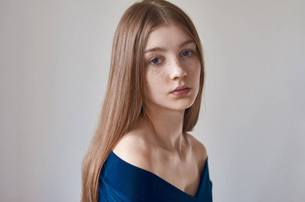 Beauty theme: portrait of a beautiful young girl with freckles on her face and wearing a blue dress on a white background in studio - Foto, imagen