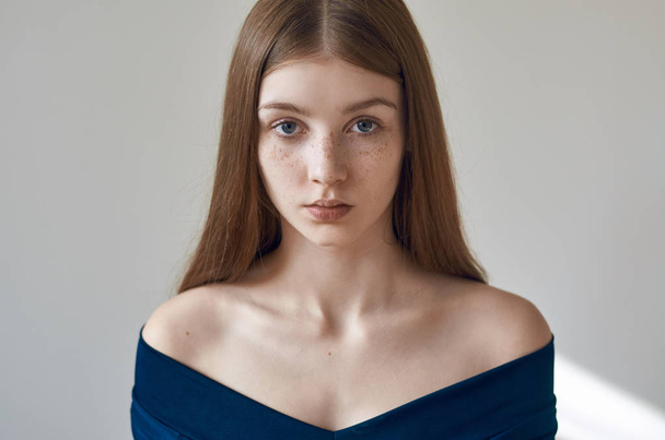 Beauty theme: portrait of a beautiful young girl with freckles on her face and wearing a blue dress on a white background in studio - Φωτογραφία, εικόνα