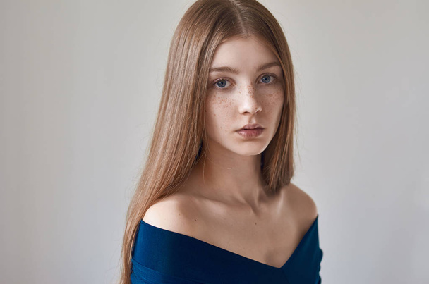 Beauty theme: portrait of a beautiful young girl with freckles on her face and wearing a blue dress on a white background in studio - Foto, Bild