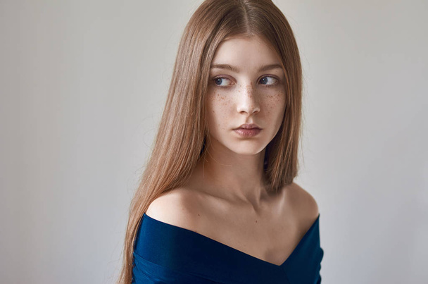 Beauty theme: portrait of a beautiful young girl with freckles on her face and wearing a blue dress on a white background in studio - Fotografie, Obrázek